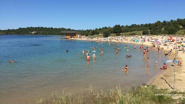 A beach with clear water, people swimming and sunbathing, and a small building in the distance.