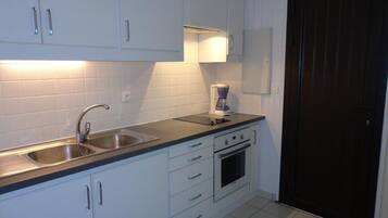 A kitchen with white cabinets, a double sink, a coffee maker, and an oven.