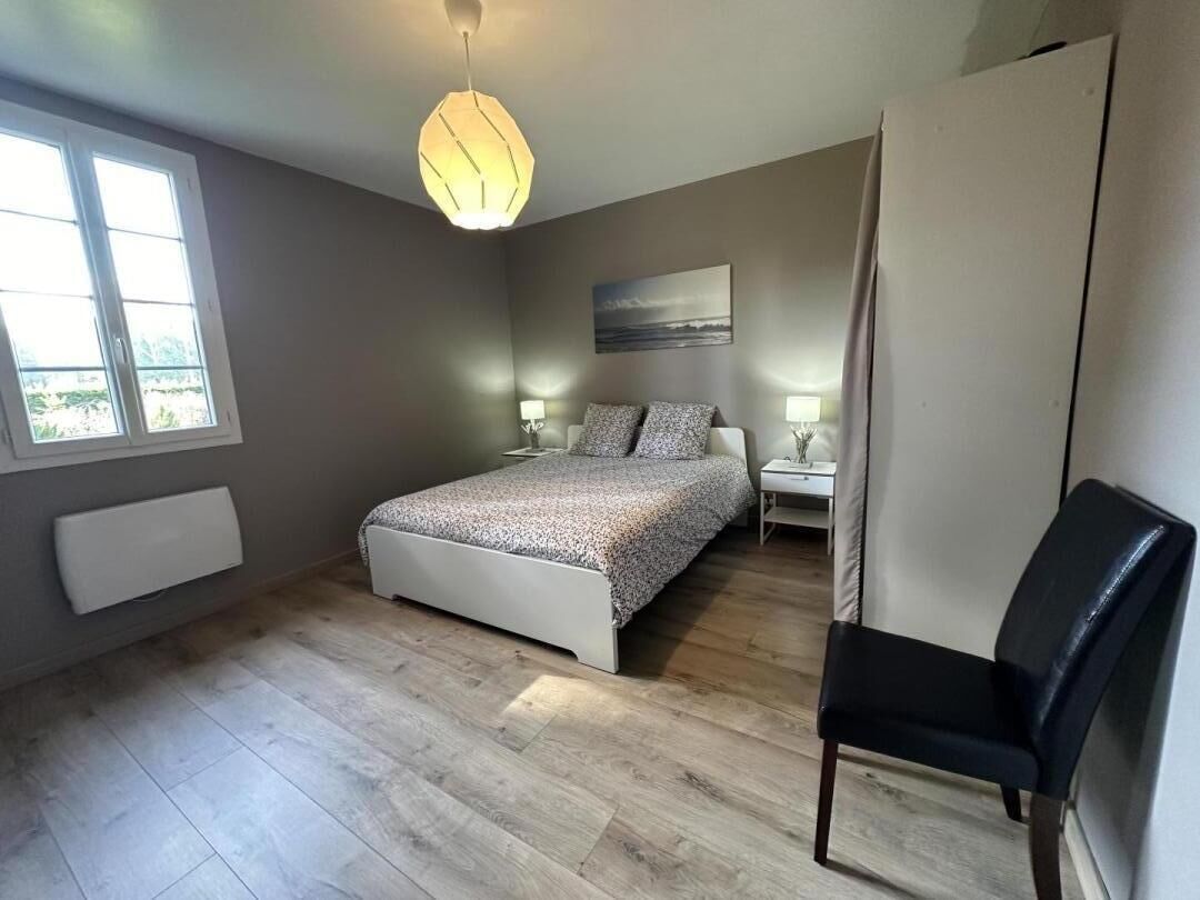 Ein Schlafzimmer mit Bett, Nachttischen, einem Sessel, einem Heizkörper, einem Fenster und einem Bild an der Wand.