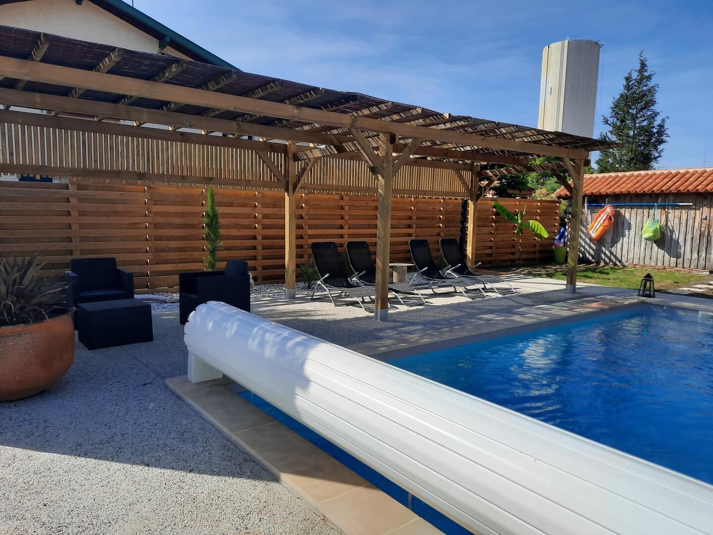 A backyard with a pool, lounge chairs, a pergola, and a wooden fence.