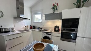 A compact kitchen with a sink, stove, microwave, and a washing machine. There is a dining table with a striped tablecloth and a wooden bowl. - Chalet Simone - ST-VINCENT-DE-TYROSSE (ST-VINCENT-DE-TYROSSE)