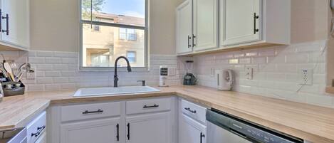 A modern kitchen with white cabinets, a dishwasher, and a window overlooking a residential area.