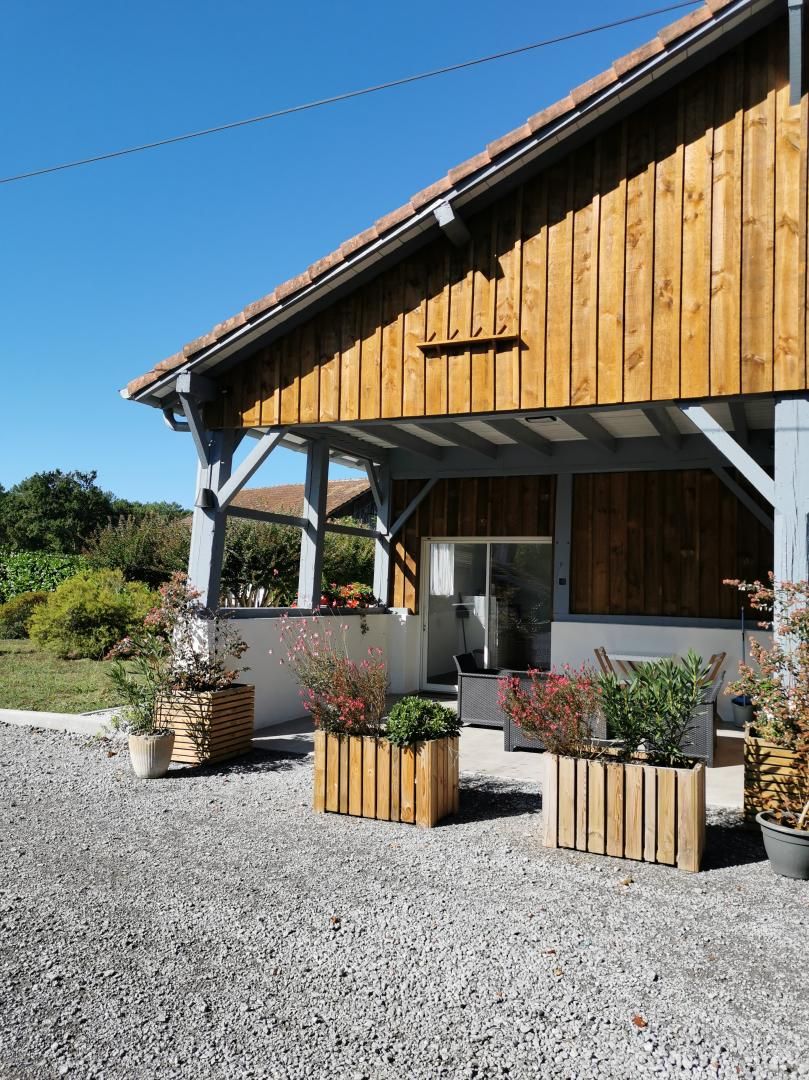 A wooden building with a covered patio area, outdoor seating, and potted plants.