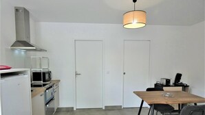 Et kompakt køkken med spiseplads, hvide skabe, en mikrobølgeovn, en brødrister og en hængende lampe.