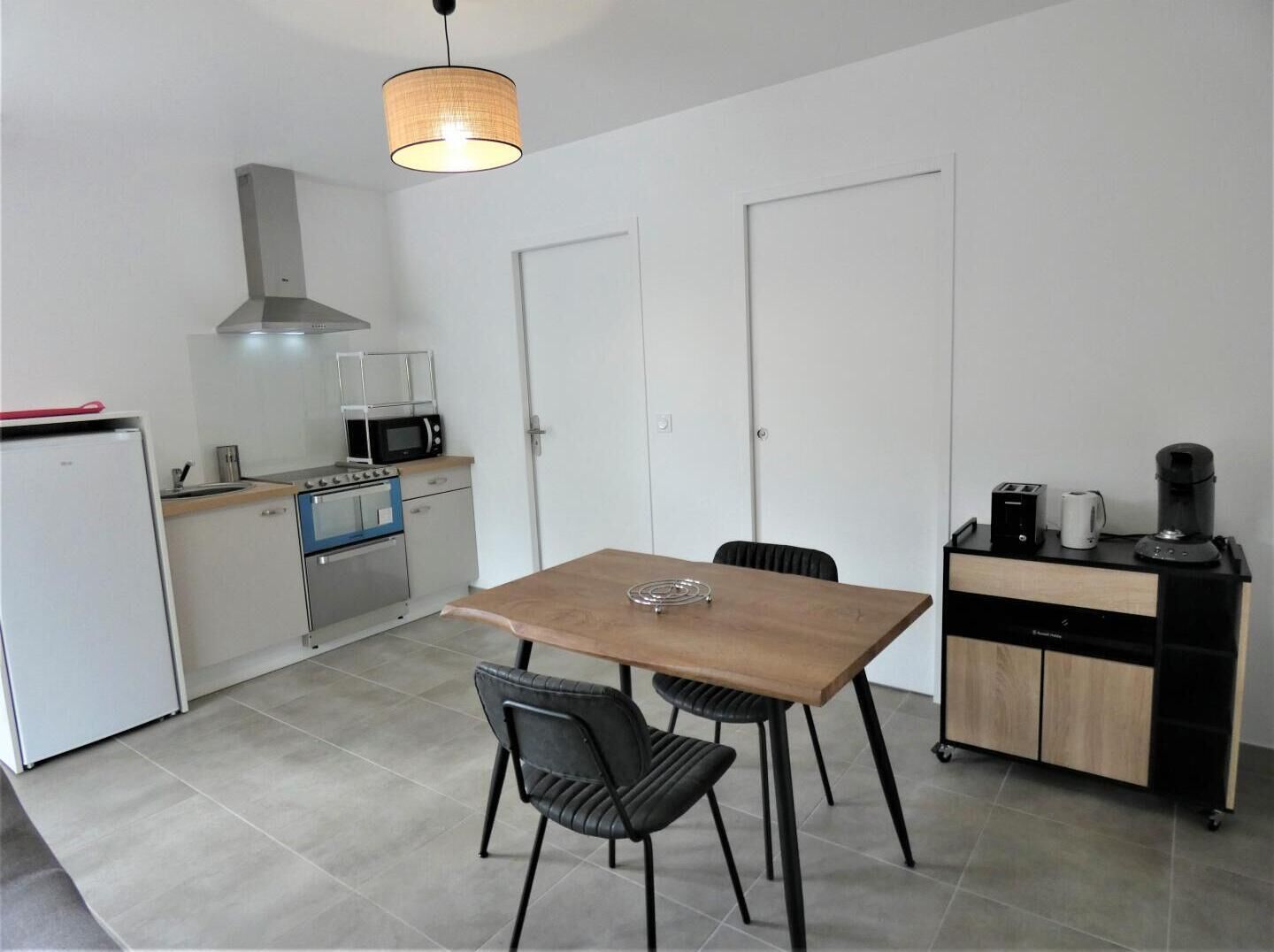 Een kleine keuken met een eettafel, stoelen, een magnetron, een fornuis en een koffieapparaat.