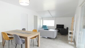 Una sala de estar moderna con comedor, un sofá gris, un televisor y una escalera apoyada en la pared.