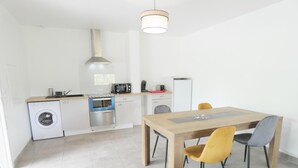 Una cocina moderna con lavadora, horno y microondas. Hay una mesa de comedor de madera con sillas y una lámpara colgante.