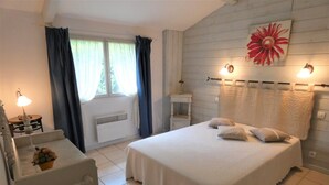 A bedroom with a bed, a bedside table, a lamp, a window with curtains, a radiator, and a wall-mounted light fixture. - Gîte de la Mousque - Castets (CASTETS)