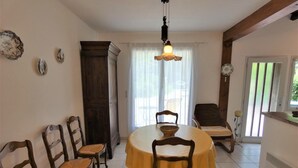 A dining area with a round table, four wooden chairs, a chandelier, and a view through a window with blinds. - Gîte de la Mousque - Castets (CASTETS)