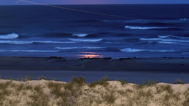 Solnedgang over havet med bølger og en sandstrand.
