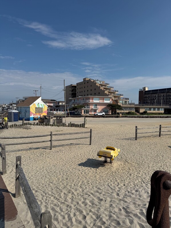 A beach with a yellow toy car, a wooden fence, and buildings in the background.
