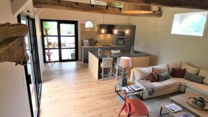 A spacious living area with a wooden floor, a sofa, a red chair, and a coffee table. There is a kitchen with a sink and a dining area with a table and chairs. - Les Ecuries du Château (BIAUDOS)