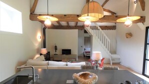 A modern kitchen with a central island, a dining area with a table and chairs, and a staircase leading to an upper level. - Les Ecuries du Château (BIAUDOS)