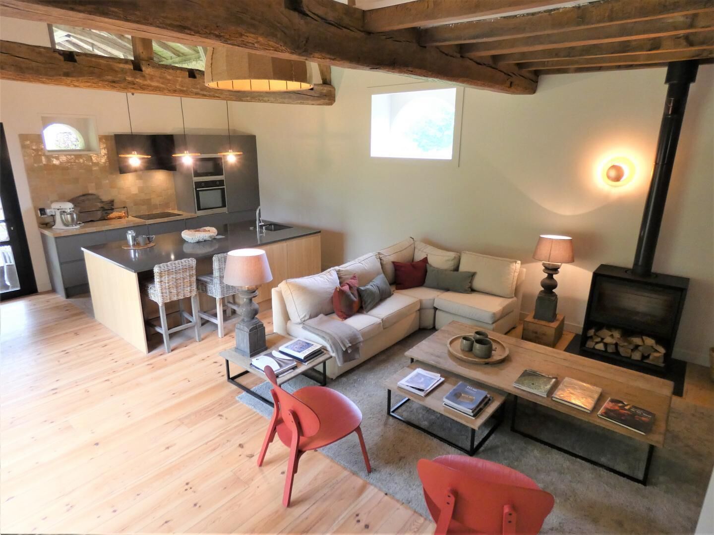 Un espace de vie moderne comprenant une cuisine, un canapé, un fauteuil rouge, une table basse et une cheminée.