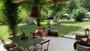 An outdoor patio with a table and chairs, surrounded by greenery and a view of a cemetery. - Les Ecuries du Château (BIAUDOS)
