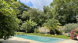 A rectangular swimming pool with a wooden deck and a lounge area with cushions. - Les Ecuries du Château (BIAUDOS)