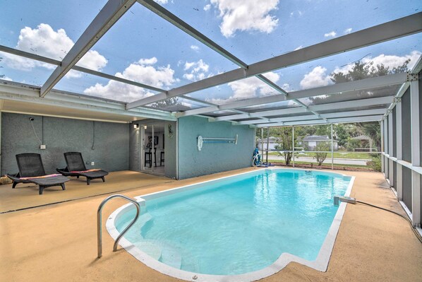 An indoor swimming pool with a glass ceiling, two lounge chairs, and a view of the outdoors. - Relaxing Port Richey Getaway w/ Lanai & Pool! (Port Richey)