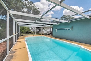 A covered swimming pool with a clear blue water, surrounded by a white metal frame and a grey wall. - Relaxing Port Richey Getaway w/ Lanai & Pool! (Port Richey)
