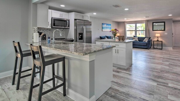 A modern kitchen with a central island, bar stools, stainless steel appliances, and a dining area with a sofa and lamp. - Relaxing Port Richey Getaway w/ Lanai & Pool! (Port Richey)