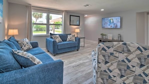 A living room with a blue sofa, a patterned armchair, and a television on the wall. - Relaxing Port Richey Getaway w/ Lanai & Pool! (Port Richey)