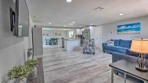 A modern living room with a blue sofa, a patterned armchair, and a table with a lamp. A kitchen and dining area are visible in the background. - Relaxing Port Richey Getaway w/ Lanai & Pool! (Port Richey)