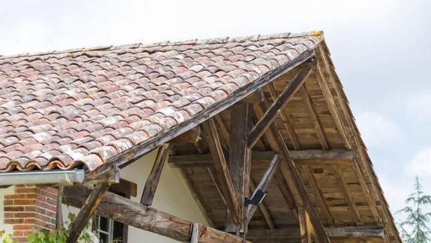 A rustic building with a tiled roof, wooden beams, and a brick facade.