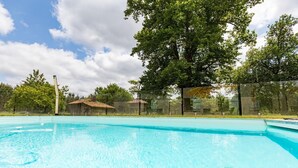 A clear swimming pool with a tiled deck, surrounded by trees and a fence.