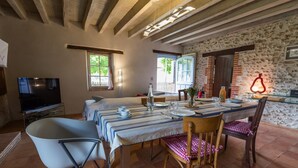 A dining area with a long table set for four, surrounded by chairs, a television, and a stone wall.