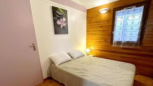 Une chambre avec un lit simple, un mur en bois, une fenêtre avec des stores et un tableau accroché au mur.