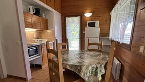 L’intérieur d’un chalet en bois comprend une table à manger, des chaises, un coin cuisine équipé d’appareils électroménagers et une fenêtre avec des rideaux.