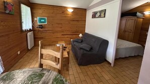 Une pièce chaleureuse avec des murs en bois, un canapé gris, une table en bois avec des chaises, un lit et un petit téléviseur fixé au mur.