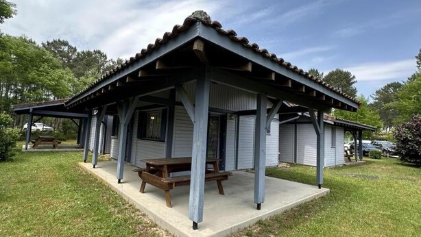 Un espace pique-nique abrité, équipé d’une table à pique-nique, situé à côté d’un bâtiment doté d’un toit à pignon.