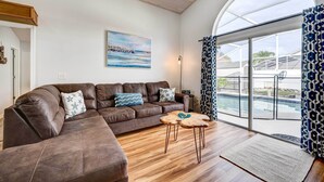 A modern living room with a brown leather sectional sofa, a wooden coffee table, and a large glass door leading to a pool area. - Kissimmee Retreat w/ Private Basketball Court! (Kissimmee)