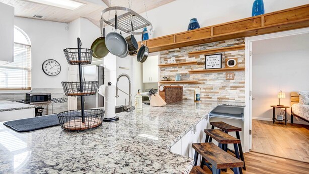 A spacious kitchen with granite countertops, hanging pots, and a clock on the wall. - Kissimmee Retreat w/ Private Basketball Court! (Kissimmee)