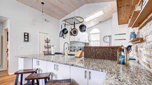 A modern kitchen with a granite countertop, hanging pots, and bar stools. - Kissimmee Retreat w/ Private Basketball Court! (Kissimmee)