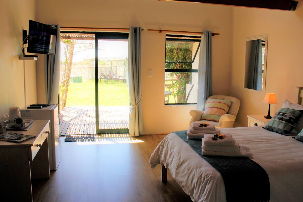 A bedroom with a bed, a desk, a chair, a TV, and a window with curtains.
