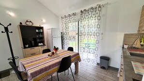 Un coin repas avec une table dressée pour deux personnes, un coin cuisine équipé d’un évier et d’une cuisinière, et un porte-manteau.