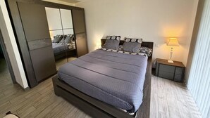 Une chambre à coucher moderne avec un grand lit, une table de chevet avec une lampe, un miroir et une armoire.