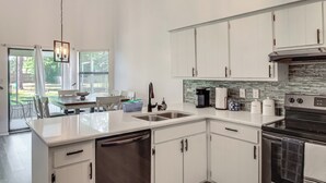 A modern kitchen with white cabinets, a dishwasher, an oven, and a coffee maker. - Navarre Home w/ Game Area + Mini Golf Course! (Navarre)