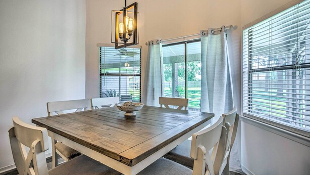 A dining area with a wooden table, white chairs, a hanging light fixture, and large windows with blinds. - Navarre Home w/ Game Area + Mini Golf Course! (Navarre)