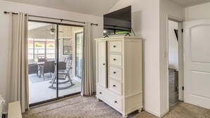 A room with a sliding glass door leading to an outdoor patio, a white cabinet, and a flat-screen TV mounted above it. - Navarre Home w/ Game Area + Mini Golf Course! (Navarre)