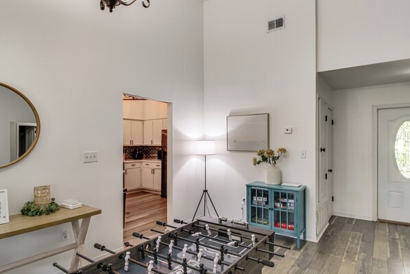 A room with a foosball table, a mirror, a lamp, a cabinet, and a door leading to another room. - Navarre Home w/ Game Area + Mini Golf Course! (Navarre)