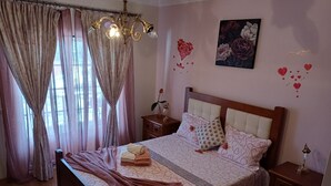 Une chambre à coucher comprenant un lit, des rideaux, un lustre, une table de chevet, une commode et un élément de décoration murale.