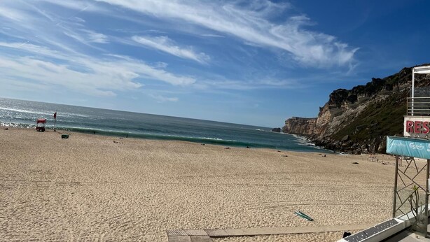 Une plage avec une falaise rocheuse, un poste de surveillance pour les sauveteurs et un panneau indiquant un complexe hôtelier.