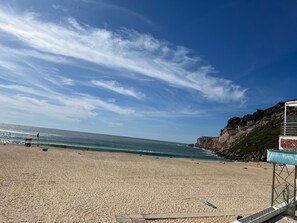 Una playa con un acantilado rocoso, una torre de salvavidas y un cartel de un resort.