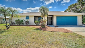 A single-story house with a blue garage door, a front lawn with a palm tree, and a clear blue sky. - 6 Mi to Dtwn Cape Coral: Home w/ Spacious Lanai! (Cape Coral)