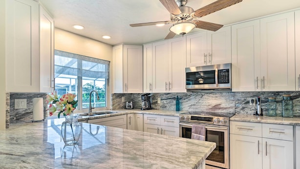 A modern kitchen with white cabinets, a marble countertop, a built-in oven, and a ceiling fan. - 6 Mi to Dtwn Cape Coral: Home w/ Spacious Lanai! (Cape Coral)
