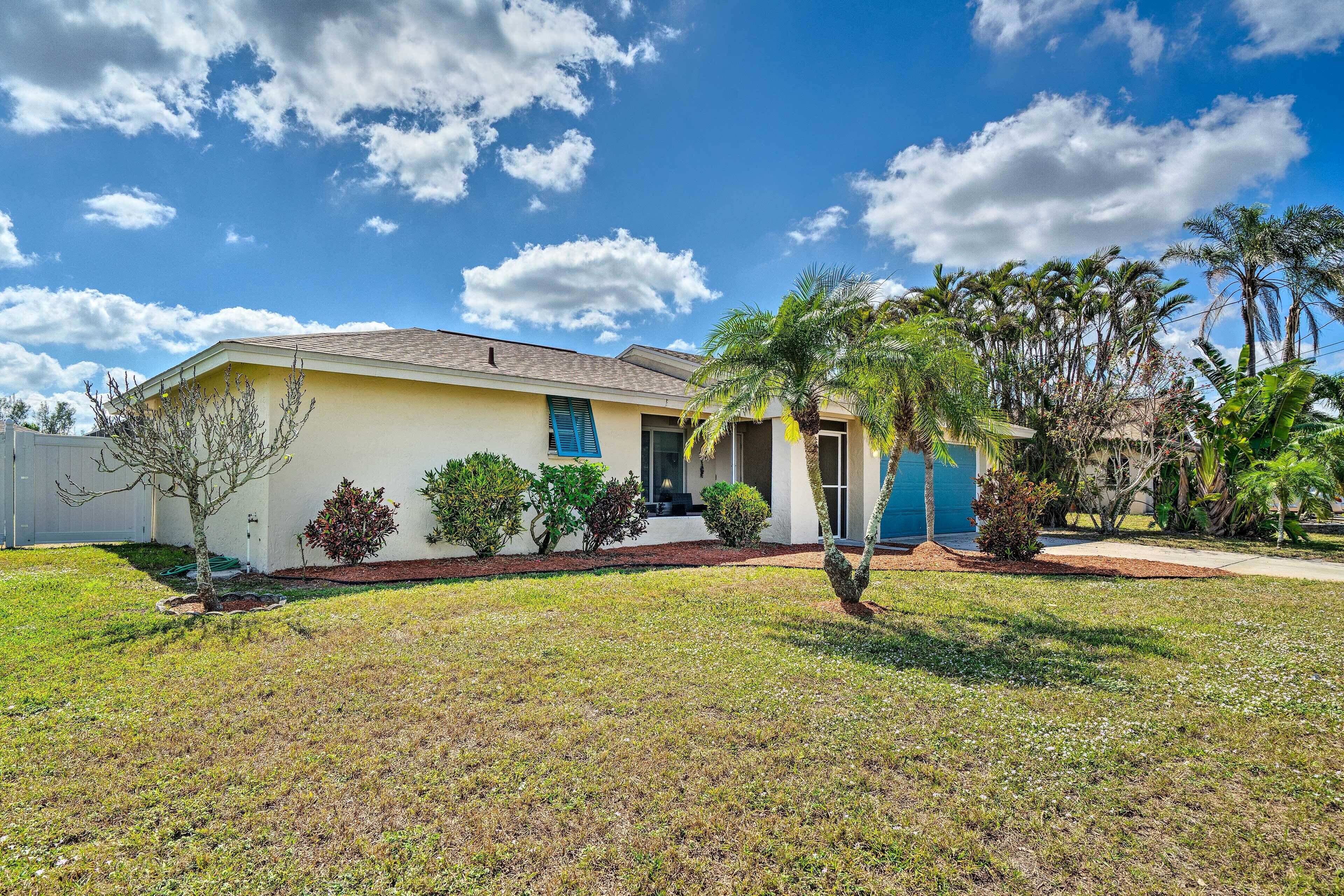 A single-story house with a yellow exterior, a blue garage door, and a front yard with grass, shrubs, and a palm tree.