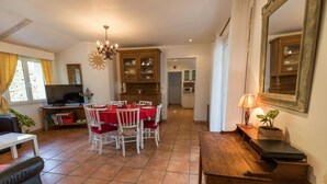 Un vaste espace de vie comprenant un coin repas avec une table dressée pour six personnes, un téléviseur et une cuisine en arrière-plan.