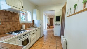 Une cuisine équipée d’une cuisinière à gaz, de meubles blancs et d’un sol carrelé.